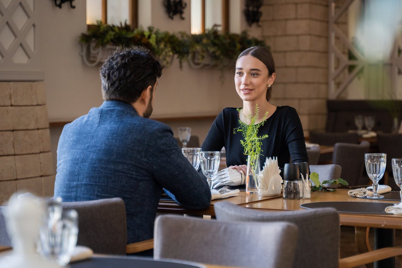 Two adults enjoying a conversation in a stylish restaurant setting, surrounded by decor and tableware.